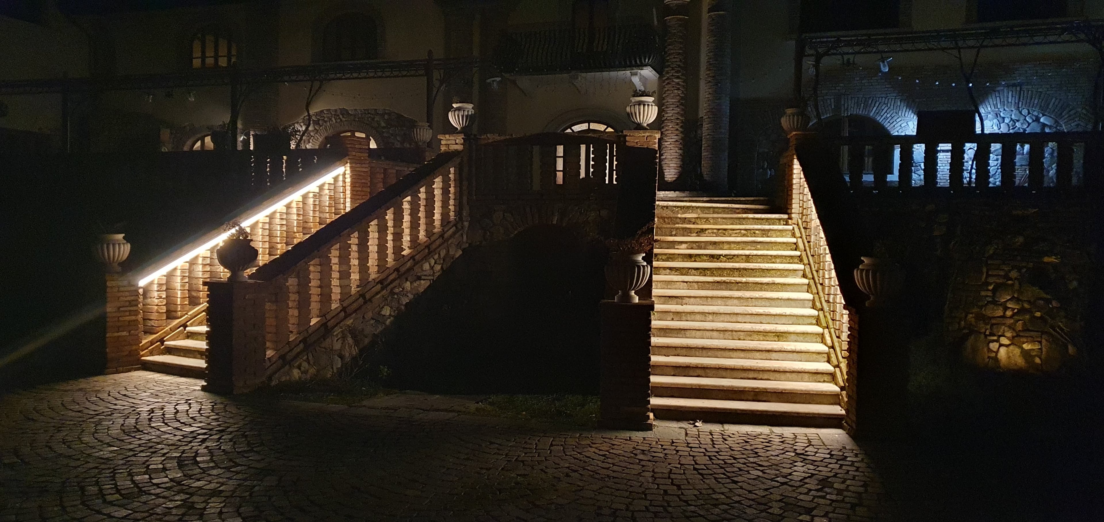 Scalinata di una villa illuminata di notte con strisce LED nascoste lungo il corrimano, intervento di illuminazione architetturale esterna realizzato da OBA Energia