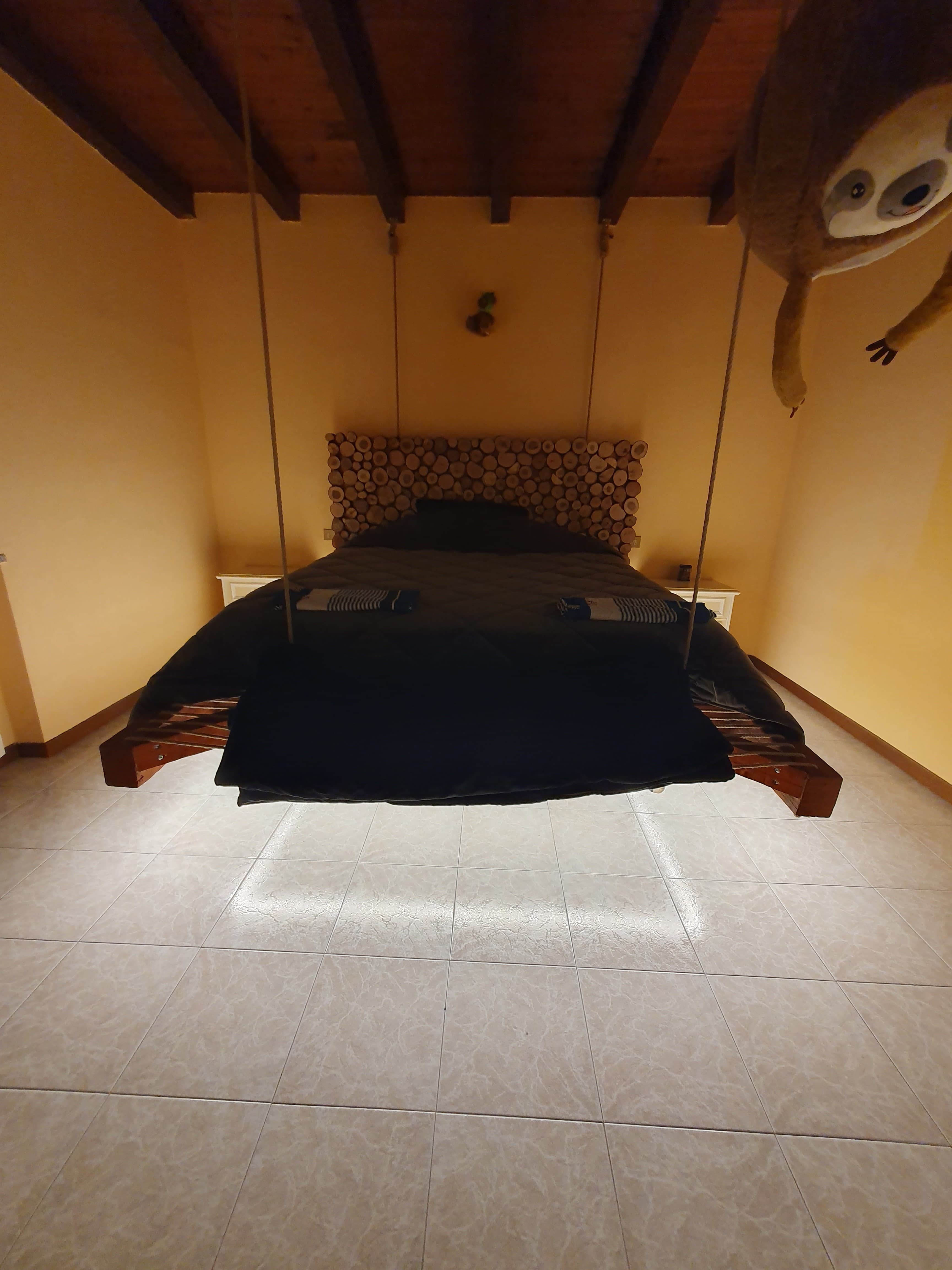 Letto matrimoniale sospeso con corde dal soffitto in legno di una mansarda, lavoro custom OBA Energia